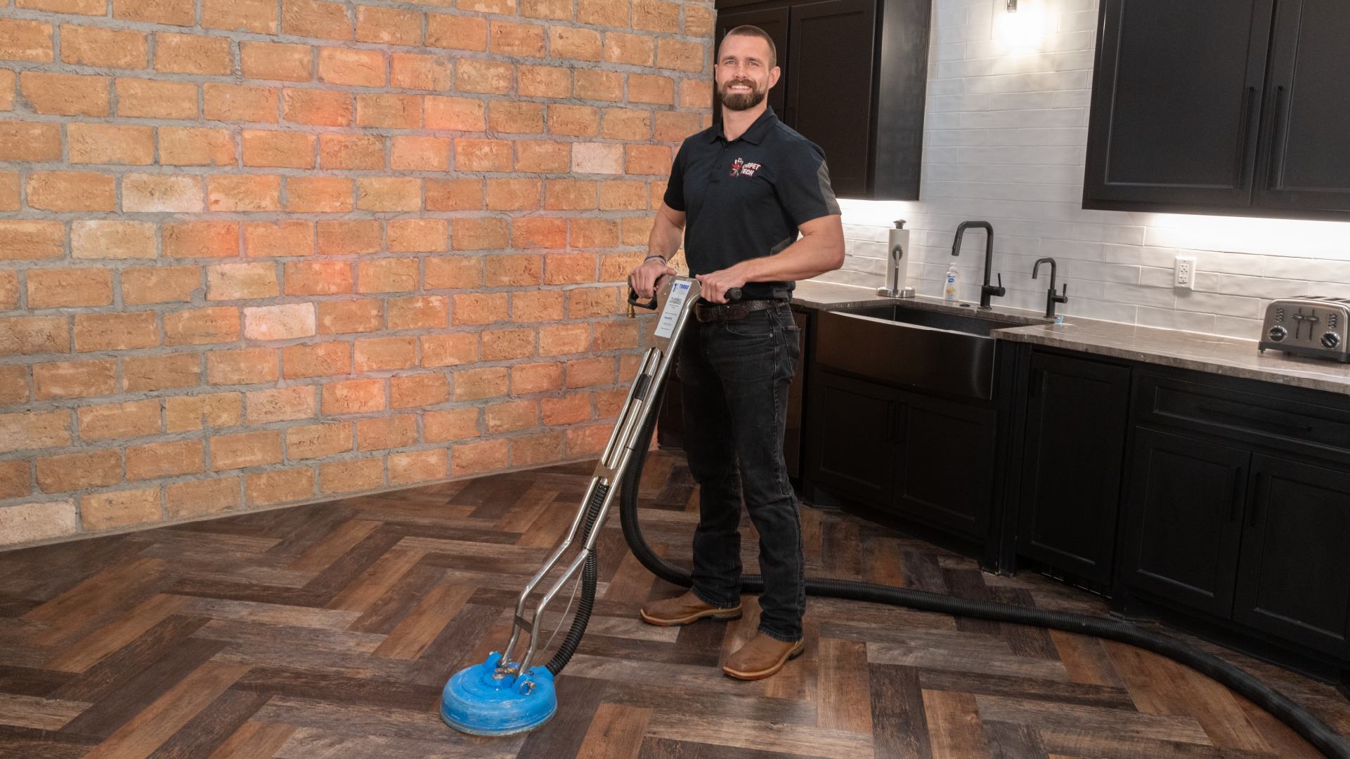 Smiling technician in a kitchen cleaning laminate flooring with a blue turbo cleaning machine