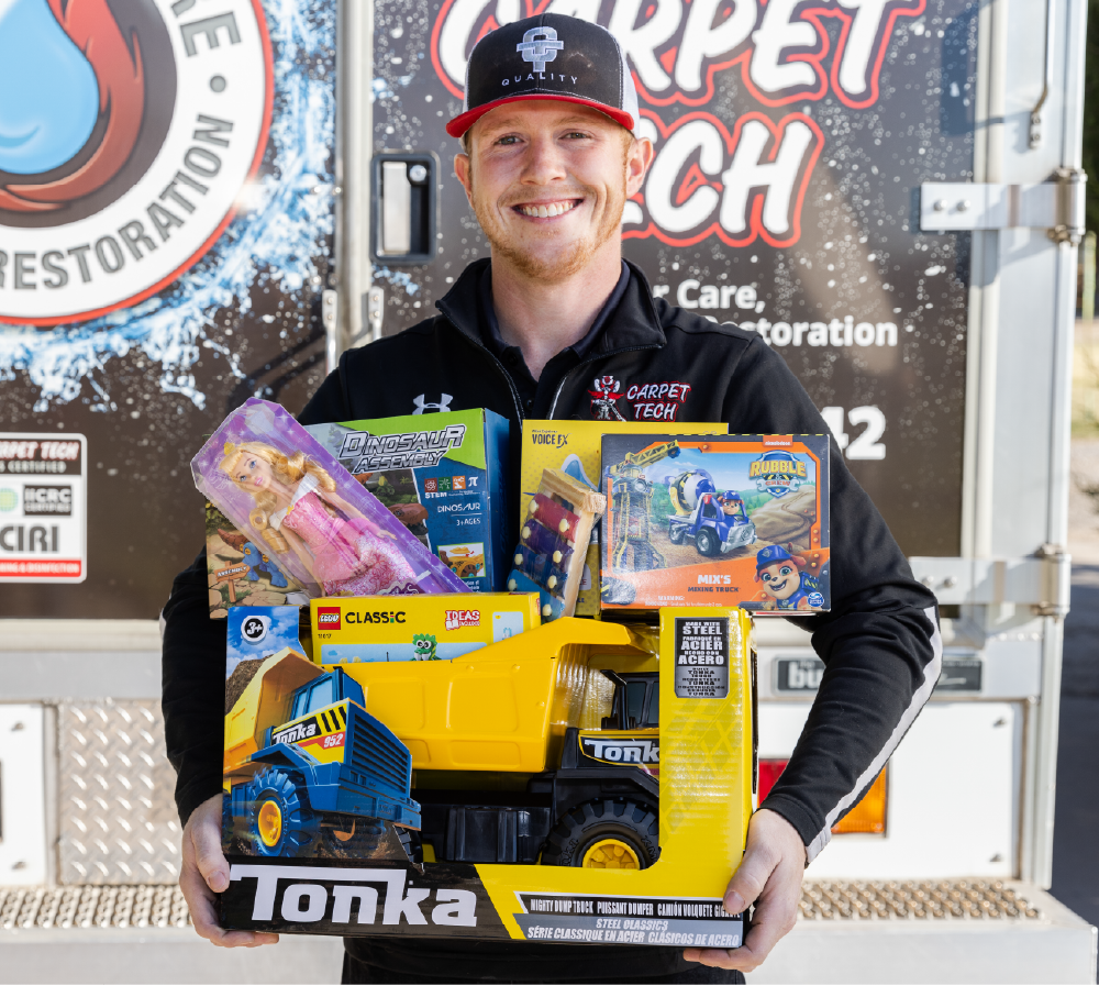 Carpet Tech technician holding an arm full of toys standing in front of a cleaning rig.