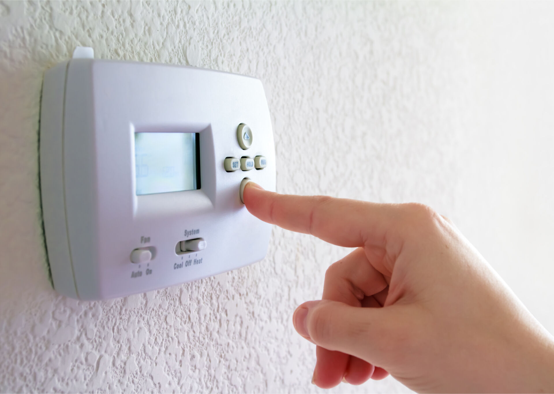 Person's hand adjusting a thermostat on the wall