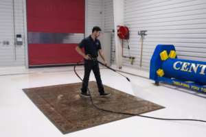 Man pressure washing rug in industrial facility
