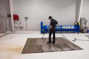 Man pressure washing rug in cleaning facility